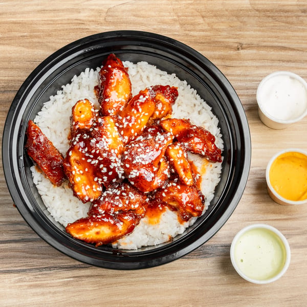 Sweet and sour chicken with sesame seeds over white rice in a black bowl, with three dipping sauces.