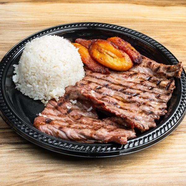 Grilled steak, white rice, and fried plantains served on a black plate on a wooden table.