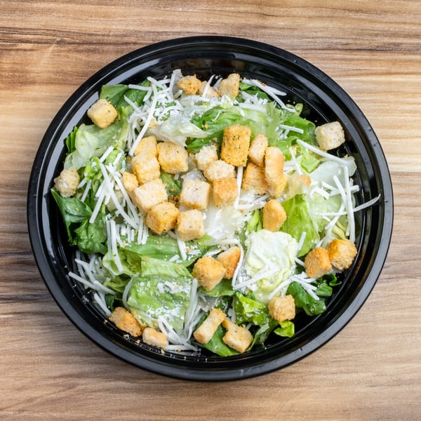 Overhead view of a Caesar salad with lettuce, croutons, and shredded cheese in a black bowl.