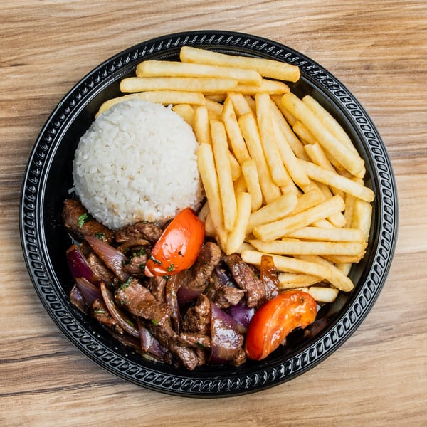 Lomo Saltado with steak, red onions, tomatoes, white rice, and french fries on a black plate.